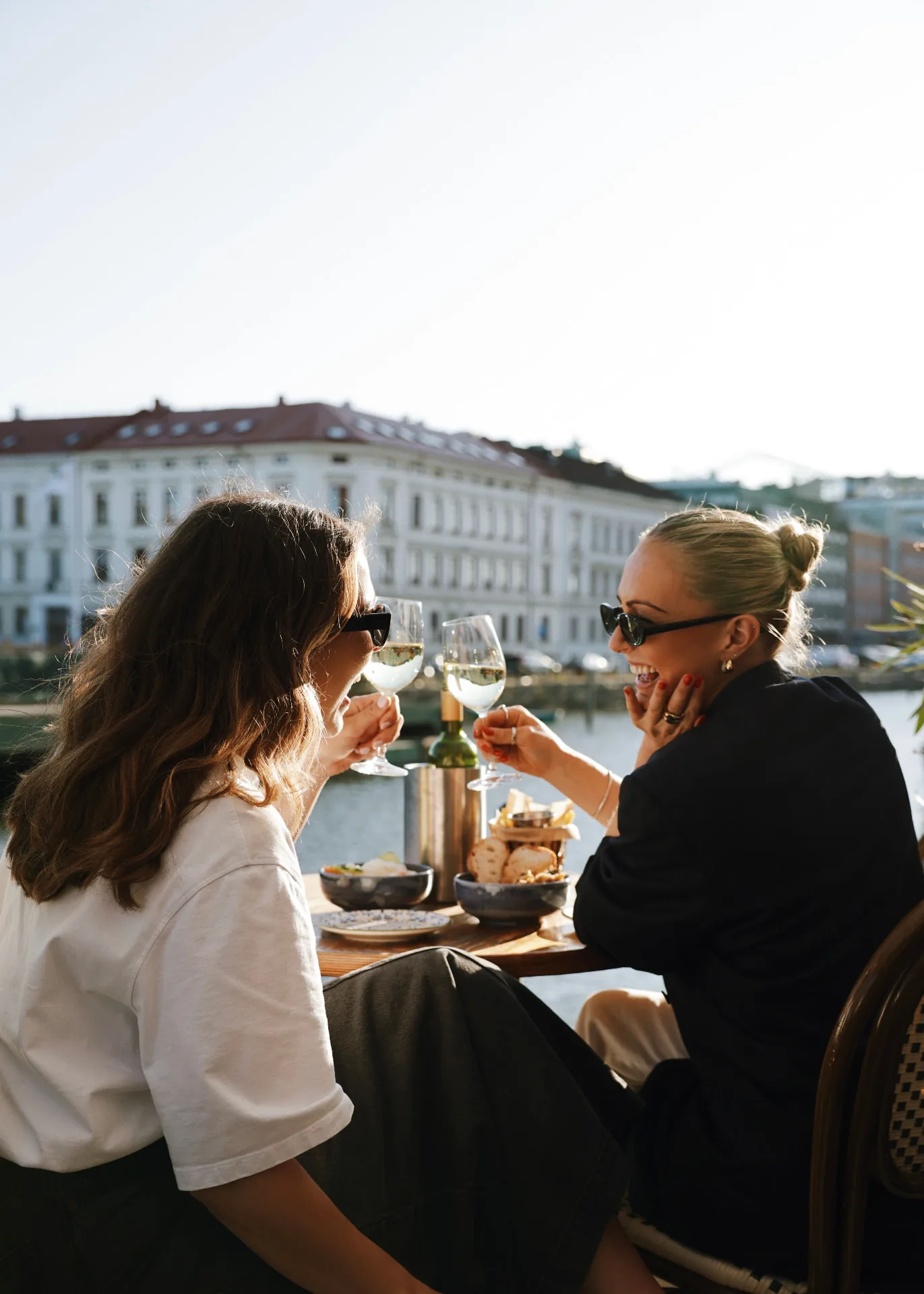 Two guests toasting on an outdoor terrace by the water